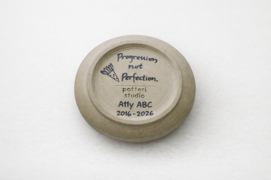 Base of coffee cup reads 'Progression not Perfection. A11y ABC 2016-2026, potteri studio'